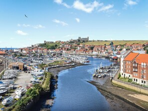 Ein Hafen mit Booten, eine Burg im Hintergrund und eine Stadt mit roten Dächern.