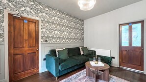 Ein Zimmer mit einem dunkelgrünen Sofa, einem Holztisch, einem gemusterten Teppich und einer dekorativen Deckenleuchte.