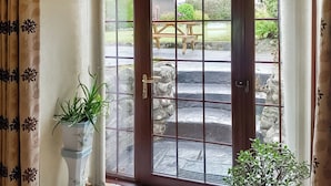 A wooden door with glass panels leading to an outdoor patio with a stone wall, a wooden bench, and potted plants. - Fox's Lair Farmhouse. (Groeslon Nr Caernarfon)