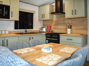 A modern kitchen with a wooden table, grey upholstered chairs, and a built-in stove. - This three-bedroom lodge at Beverley Holiday Park, Paignton. (Paignton)