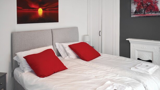 Ein Doppelbett mit weißer Bettwäsche und roten Kissen, ein weißer Nachttisch und ein weißer Kamin.