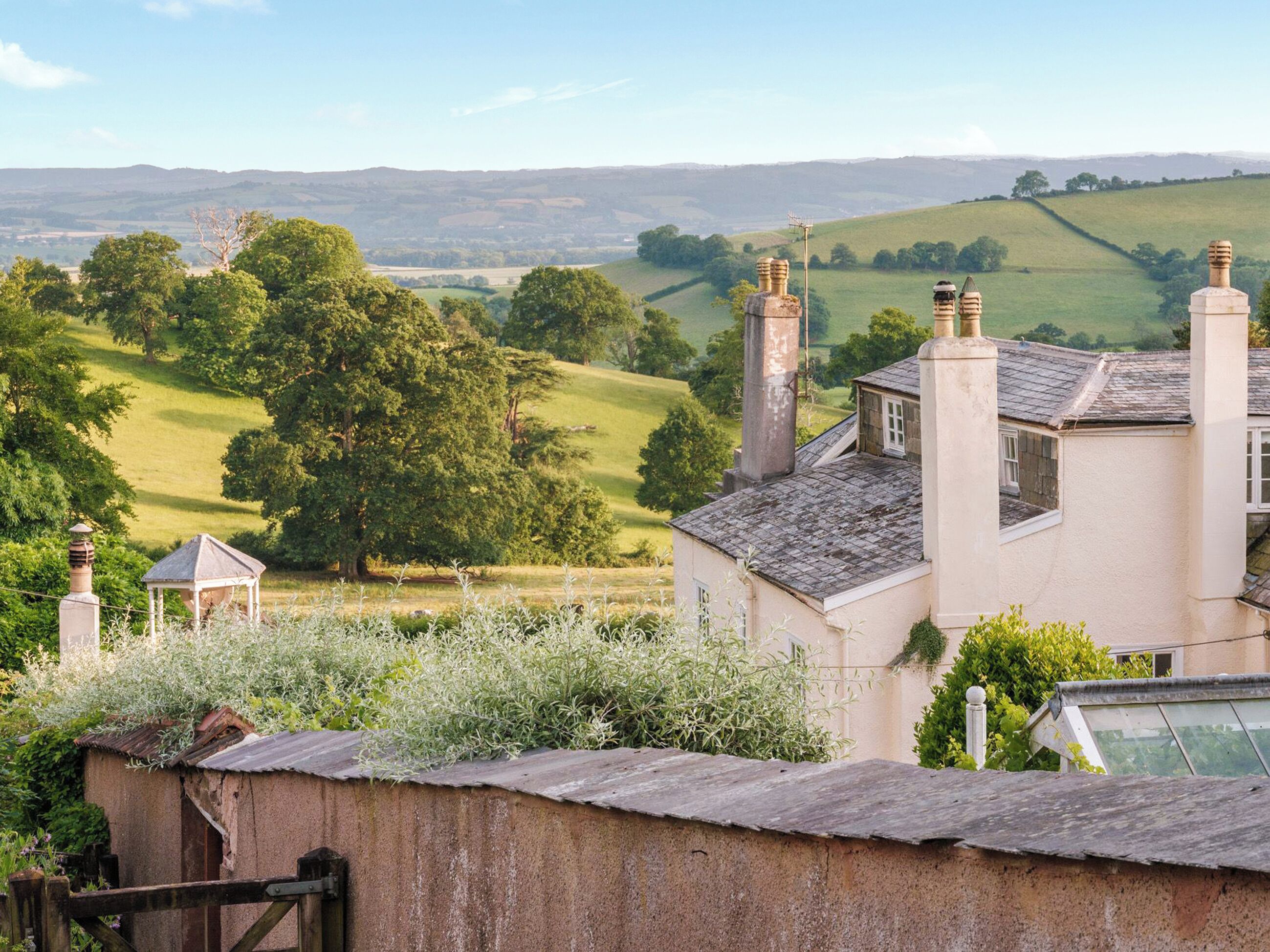 Una casa rural con jardín, un pequeño pabellón y vistas a colinas ondulantes.