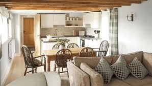 Ein gemütliches Wohnzimmer mit einer Couch und Sesseln, ein Essbereich mit Tisch und Stühlen und eine Küche im Hintergrund.
