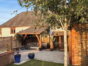 Een bakstenen huis met een houten veranda, een stenen terras en een kleine tuin met potplanten.