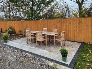 A patio with a wooden table and chairs, surrounded by a wooden fence and potted plants.