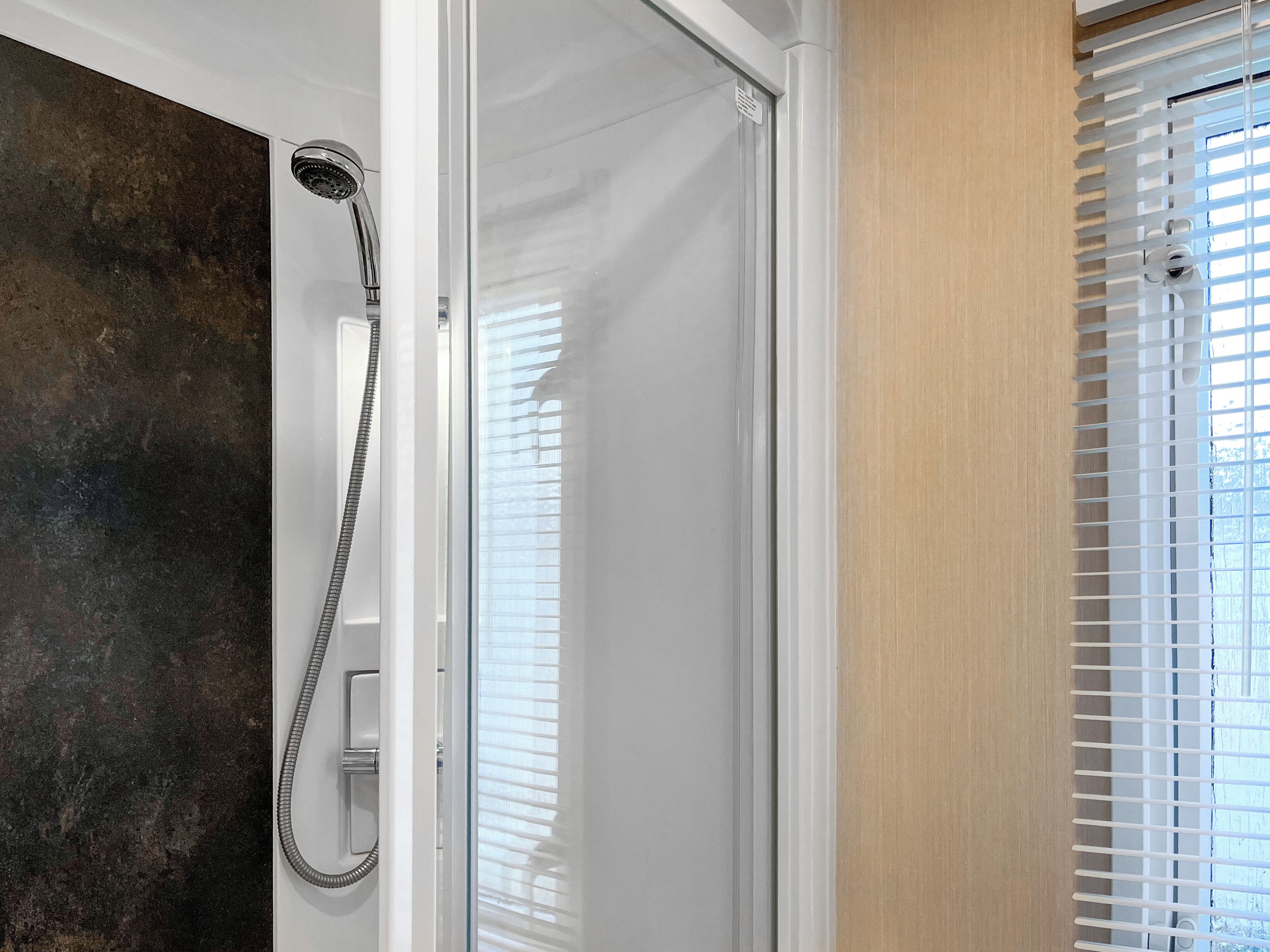 Ducha con manguera, puerta de cristal y ventana con persianas.