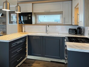 A modern kitchen with dark cabinets, a window above the sink, a built-in oven, and a stainless steel range hood. - 2 bedroom accommodation in Filey (Filey)