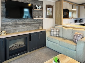 Una sala de estar moderna con televisor de pantalla plana, chimenea, sofá y una zona de cocina con microondas.