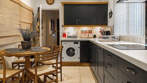 Een praktische keuken met een wasmachine, houten stoelen en een eettafel.