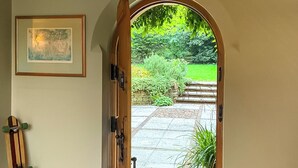An arched doorway leading to a garden with a stone pathway, a framed picture on the wall, and a skateboard leaning against the wall. - 4 bedroom accommodation in Olney (Olney)