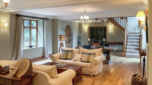 A spacious living room with a wooden floor, a sofa set, a dining table, and a staircase leading to another level. - 4 bedroom accommodation in Olney (Olney)