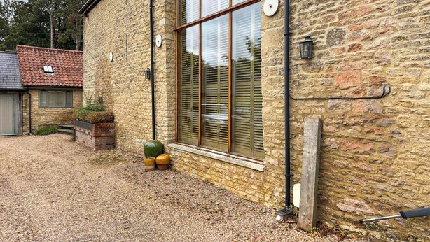 A stone building with a large window, a gravel driveway, and a small garden area with pots. - 4 bedroom accommodation in Olney (Olney)
