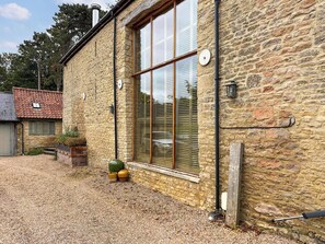A stone building with a large window, a gravel driveway, and a small garden area with pots. - 4 bedroom accommodation in Olney (Olney)