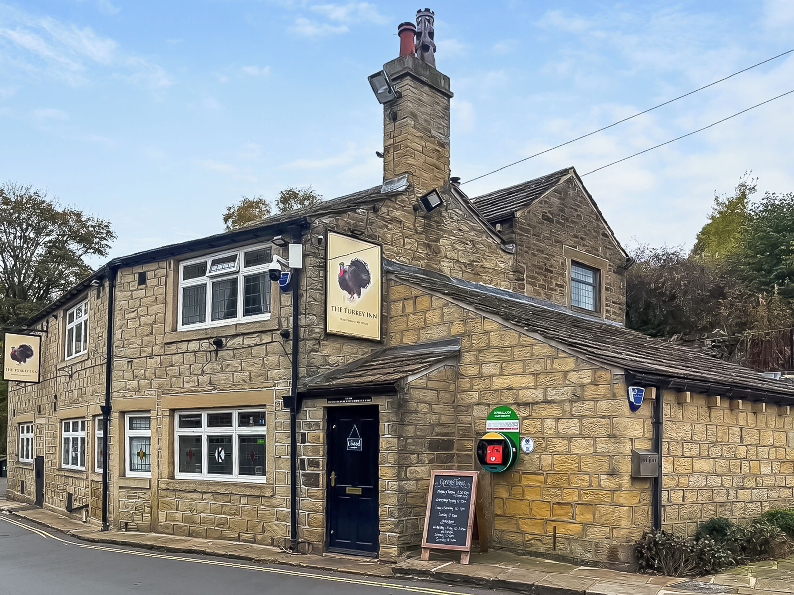 A stone building with a sign reading 'The Turkey Inn,' a closed door, and a chalkboard with opening times.