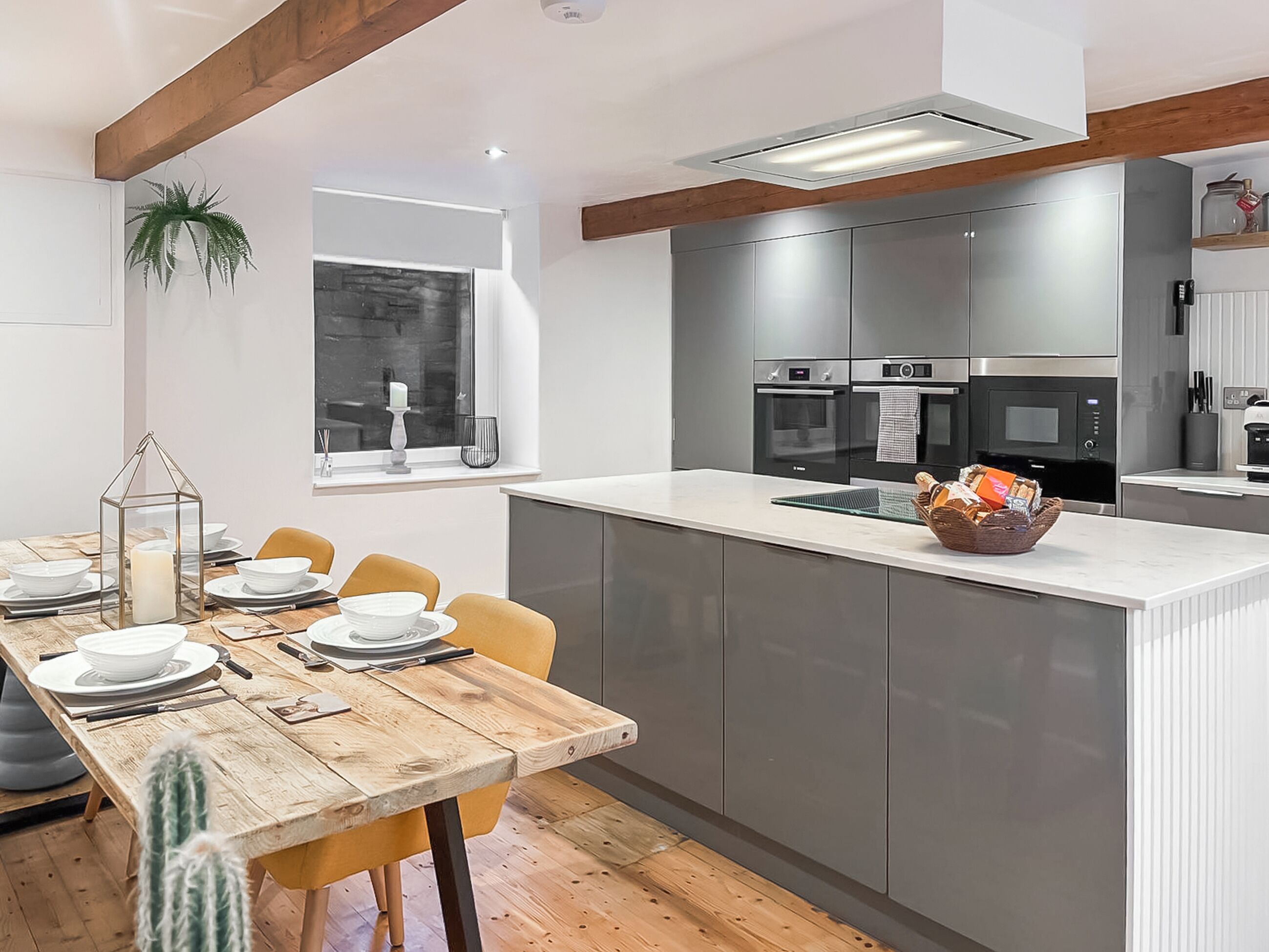 A modern kitchen with grey cabinets, a wooden dining table, and a window with a view.
