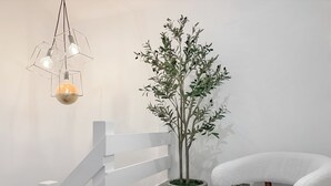 Una silla blanca, una planta en maceta y una lámpara con forma geométrica.