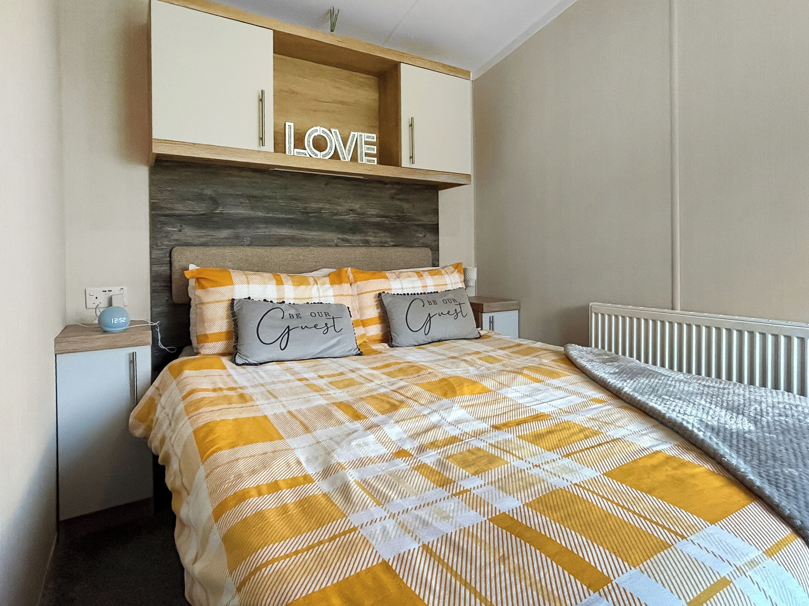 A bedroom with a bed, a nightstand, a wooden headboard, and a shelf with a 'LOVE' sign.