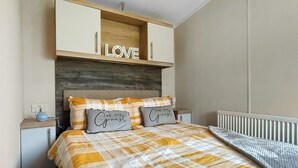 Une chambre à coucher avec un lit, une table de chevet, une tête de lit en bois et une étagère ornée d’un panneau indiquant le mot « AMOUR ».