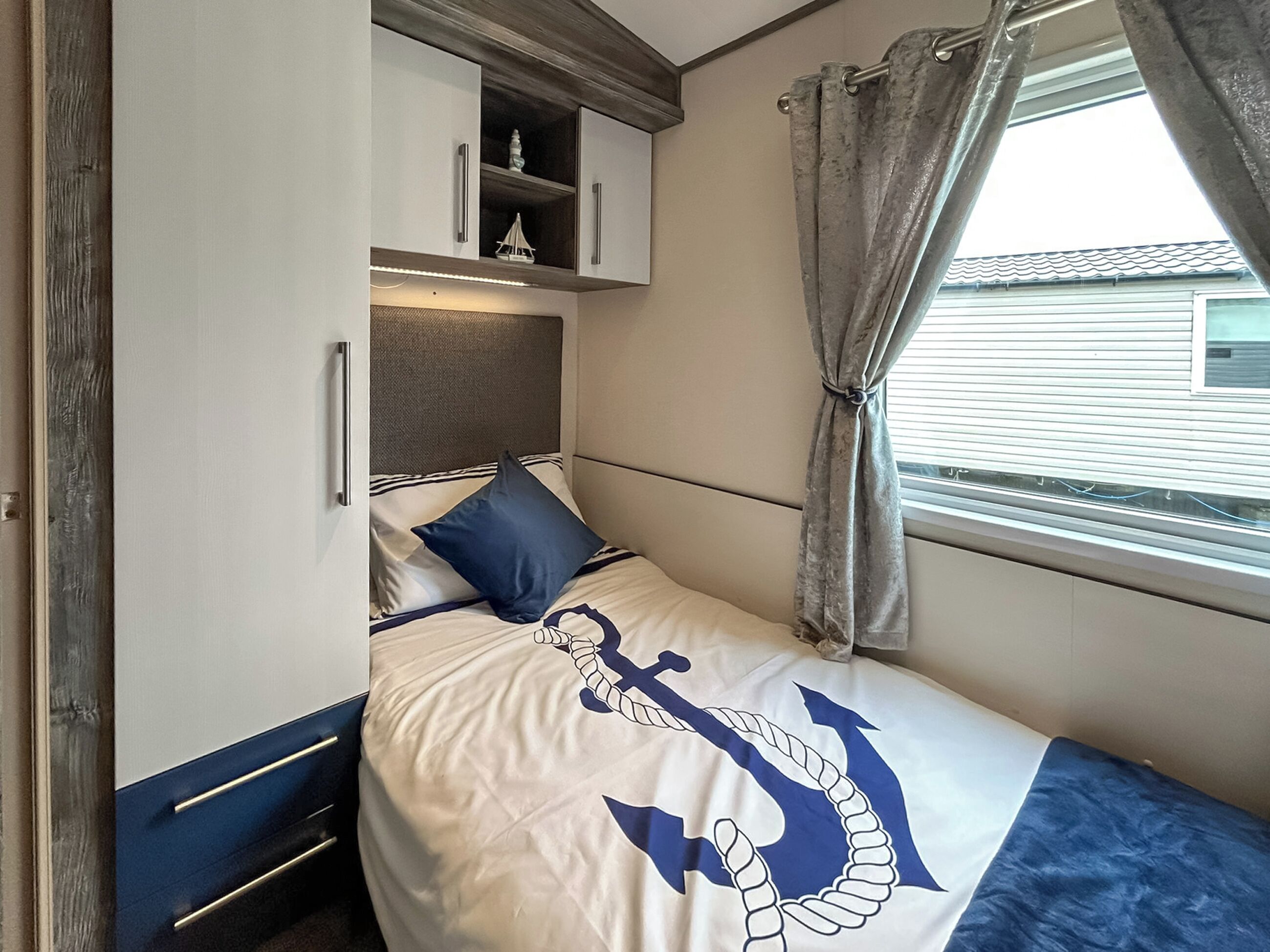 A bedroom with a bed, a headboard, a window with curtains, and a shelf with decorative items.