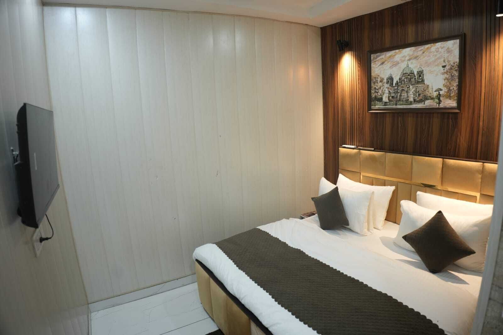 A hotel room with a bed, a TV, and a painting on the wall.