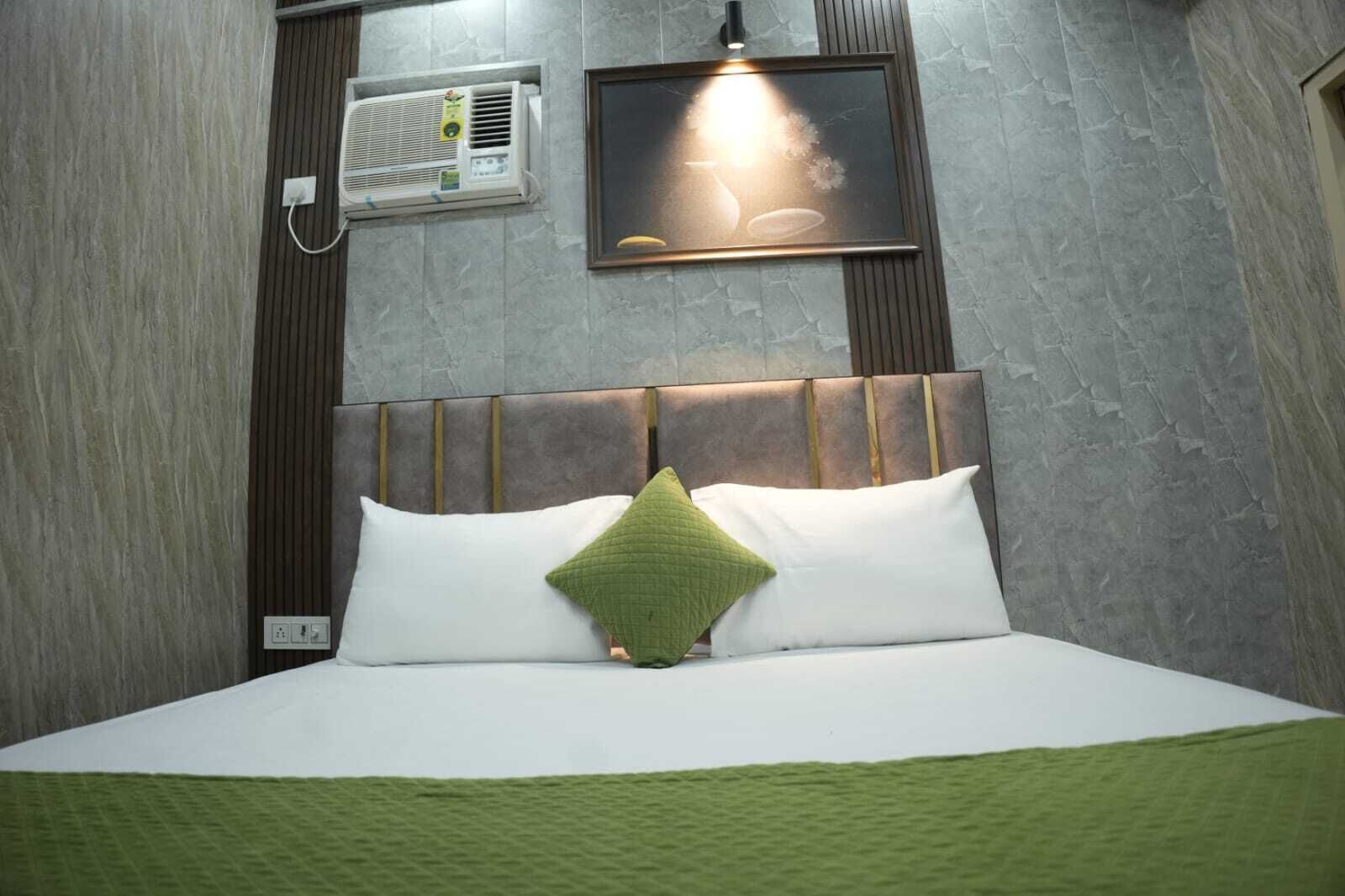 A hotel room with a bed, a wall-mounted air conditioner, and a framed picture above the bed.