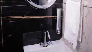 Un baño con lavamanos blanco, un espejo redondo y un perchero para toallas.