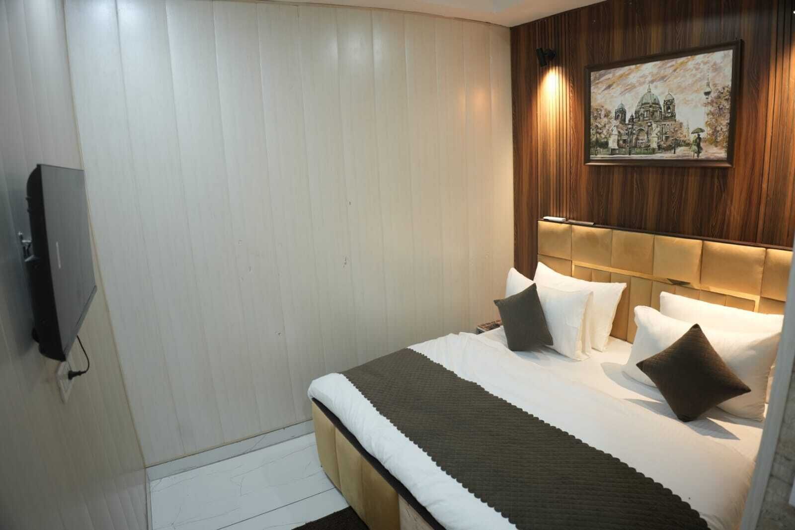 A hotel room with a bed, a television, a painting on the wall, and a wooden headboard.