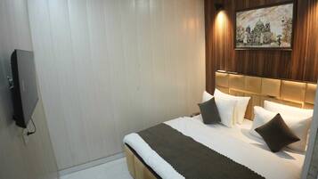 A hotel room with a bed, a television, a painting on the wall, and a wooden headboard.