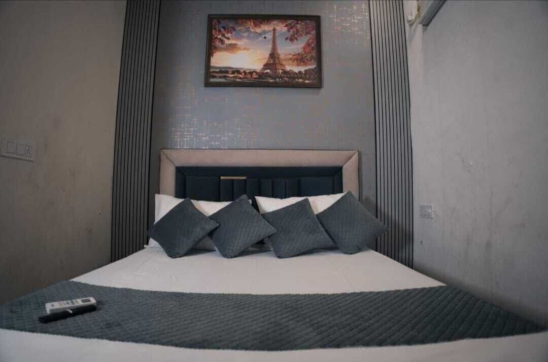 Een hotelkamer met een bed, een afstandsbediening en een schilderij van de Eiffeltoren aan de muur.