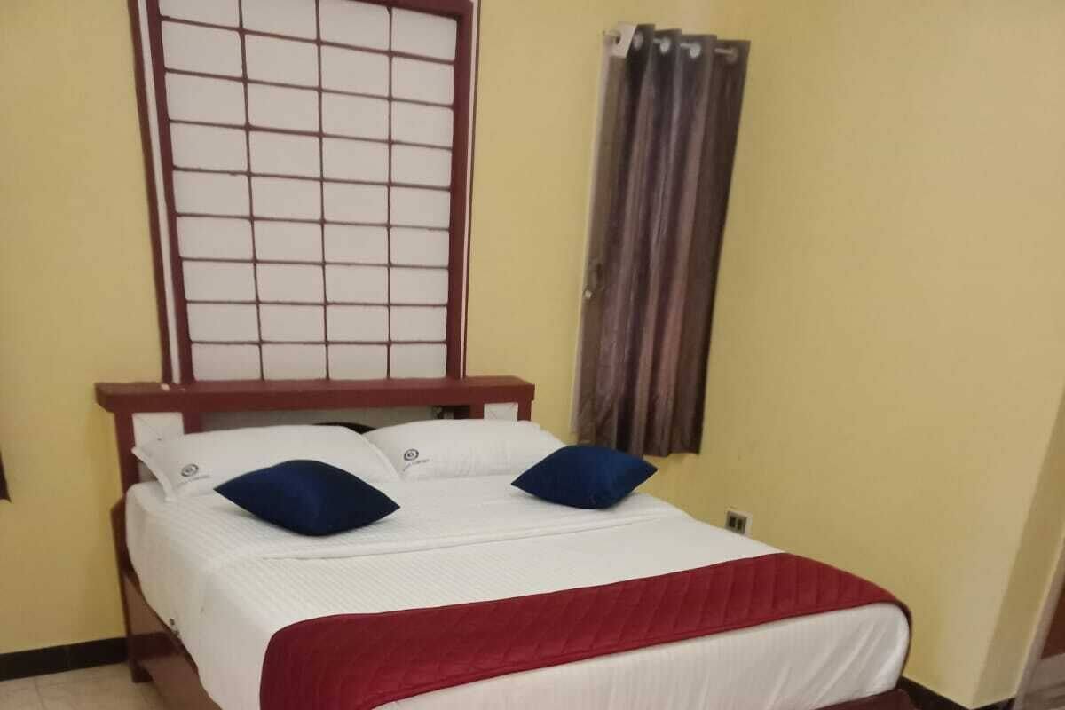 A single bed with a wooden frame, white bedding, and two blue pillows.