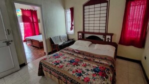 A bedroom with a bed, a wooden headboard, a window with bars, and a door leading to another room. - Sunshine Royale (Kodaikanal)