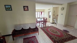 A living room with a sofa, a dining table, and chairs. There are two rugs on the floor. - Sunshine Royale (Kodaikanal)