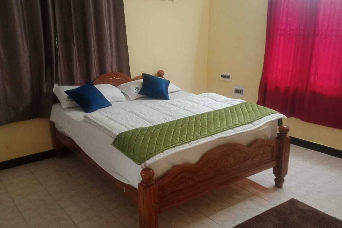 A bedroom with a bed, curtains, a wall-mounted air conditioner, a small decorative item, and a tiled floor.