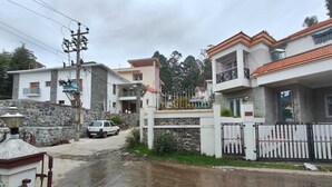 A residential street with houses, a white car parked on the side, and a wet road. - Sunshine Royale (Kodaikanal)