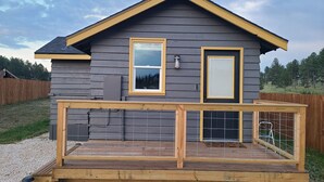 Uma casa de dois andares com fachada cinza escura, telhado amarelo e deck de madeira com guarda-corpo.