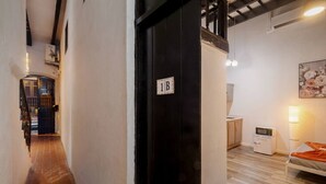 A hallway leading to a bedroom with a bed, a nightstand, a lamp, and a microwave. There is a door with a sign indicating room number 1B. - Il Rifugio Nascosto | Somewhere In Heaven (San Juan)