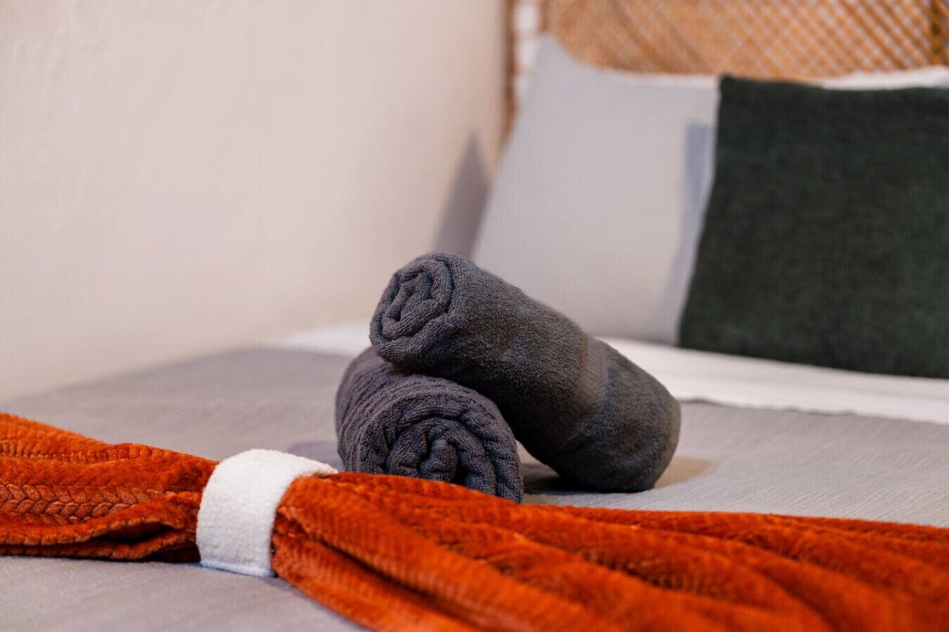 A bed with grey sheets, a grey pillow, and a dark grey blanket rolled up at the foot.