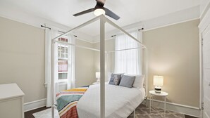 Ein Himmelsbett mit Baldachin, ein Nachttisch mit Lampe und ein Fenster mit Vorhängen.