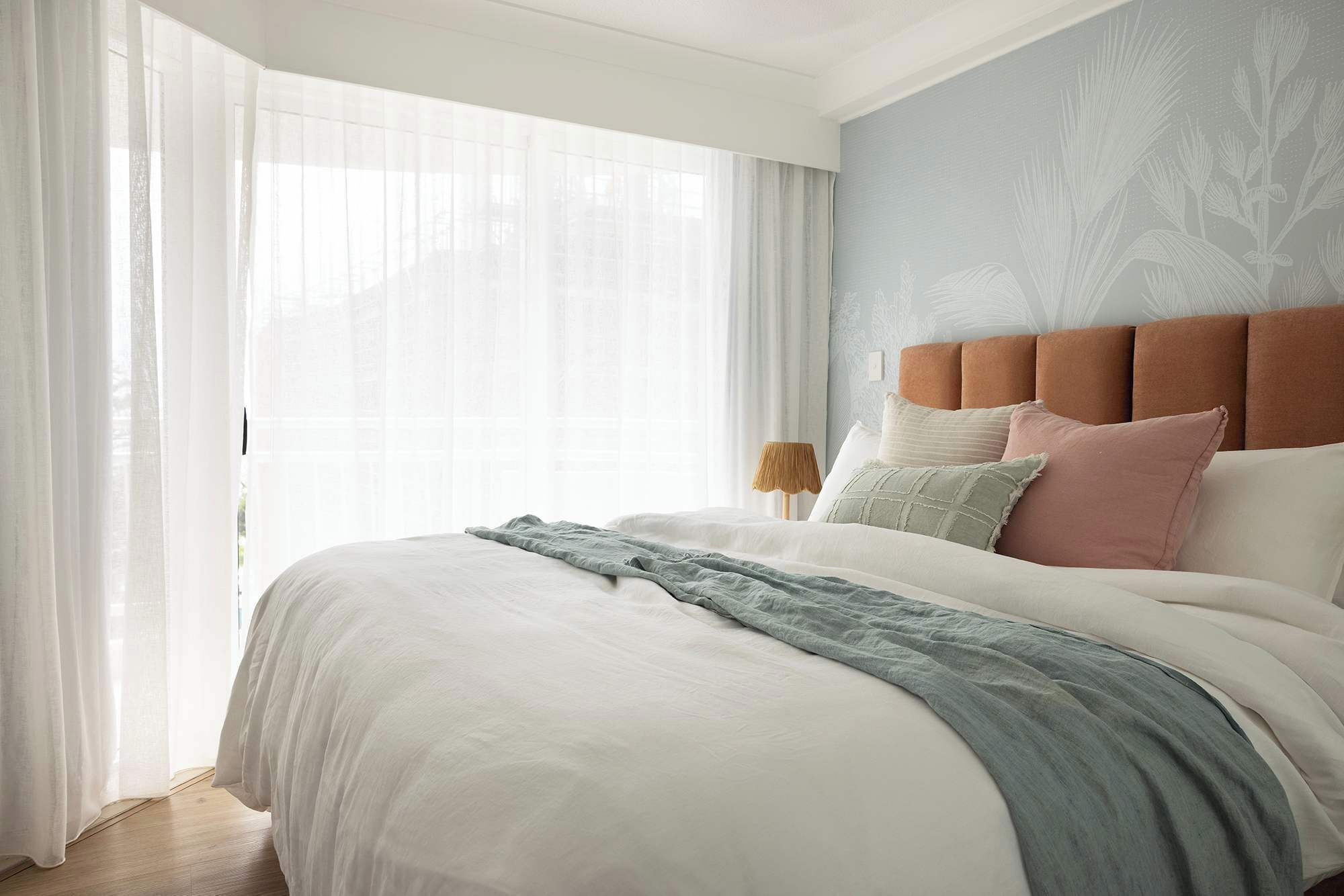 A bedroom with a large bed, a headboard, and a window with sheer curtains.