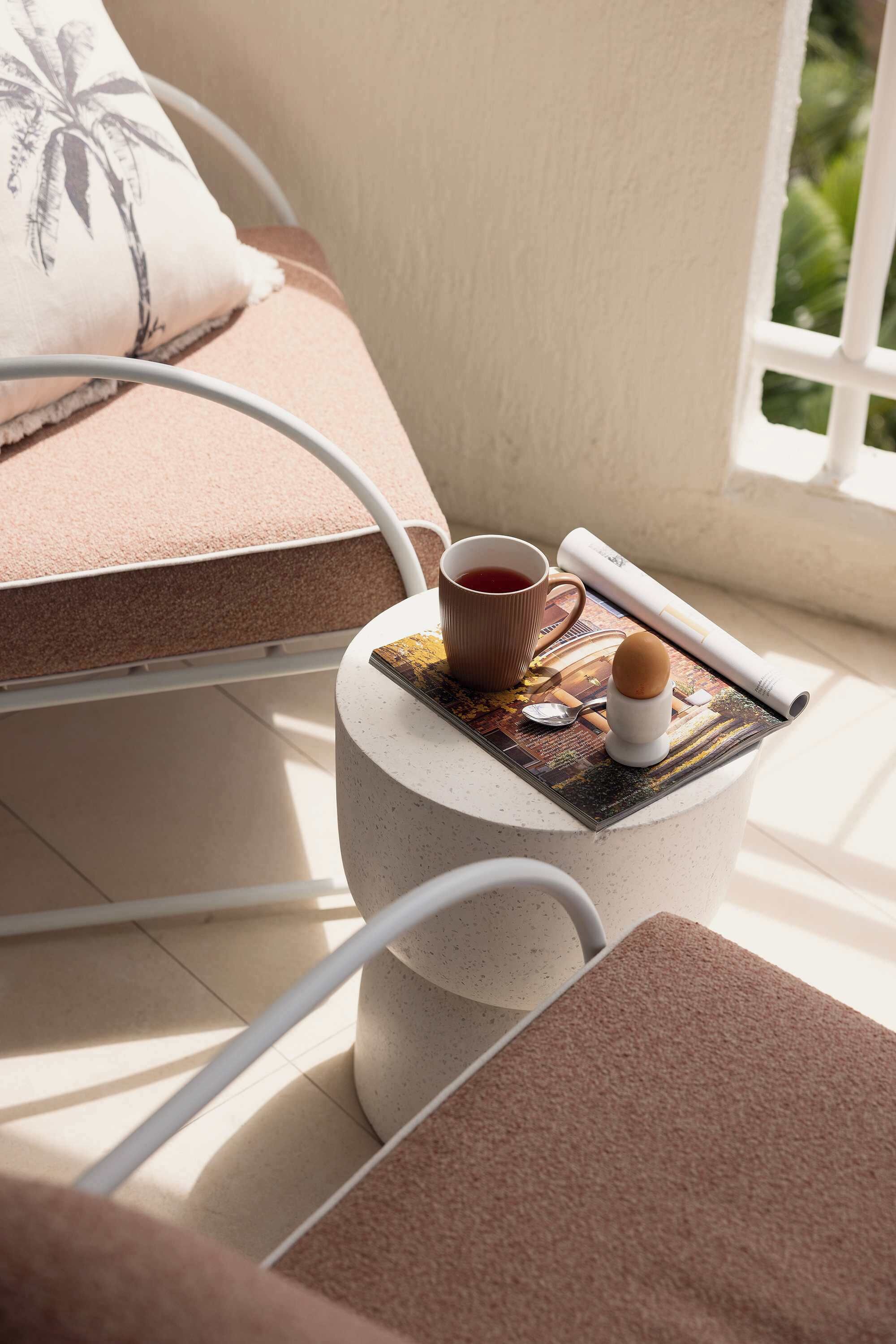 A small round table with a magazine, a cup, and a spoon.
