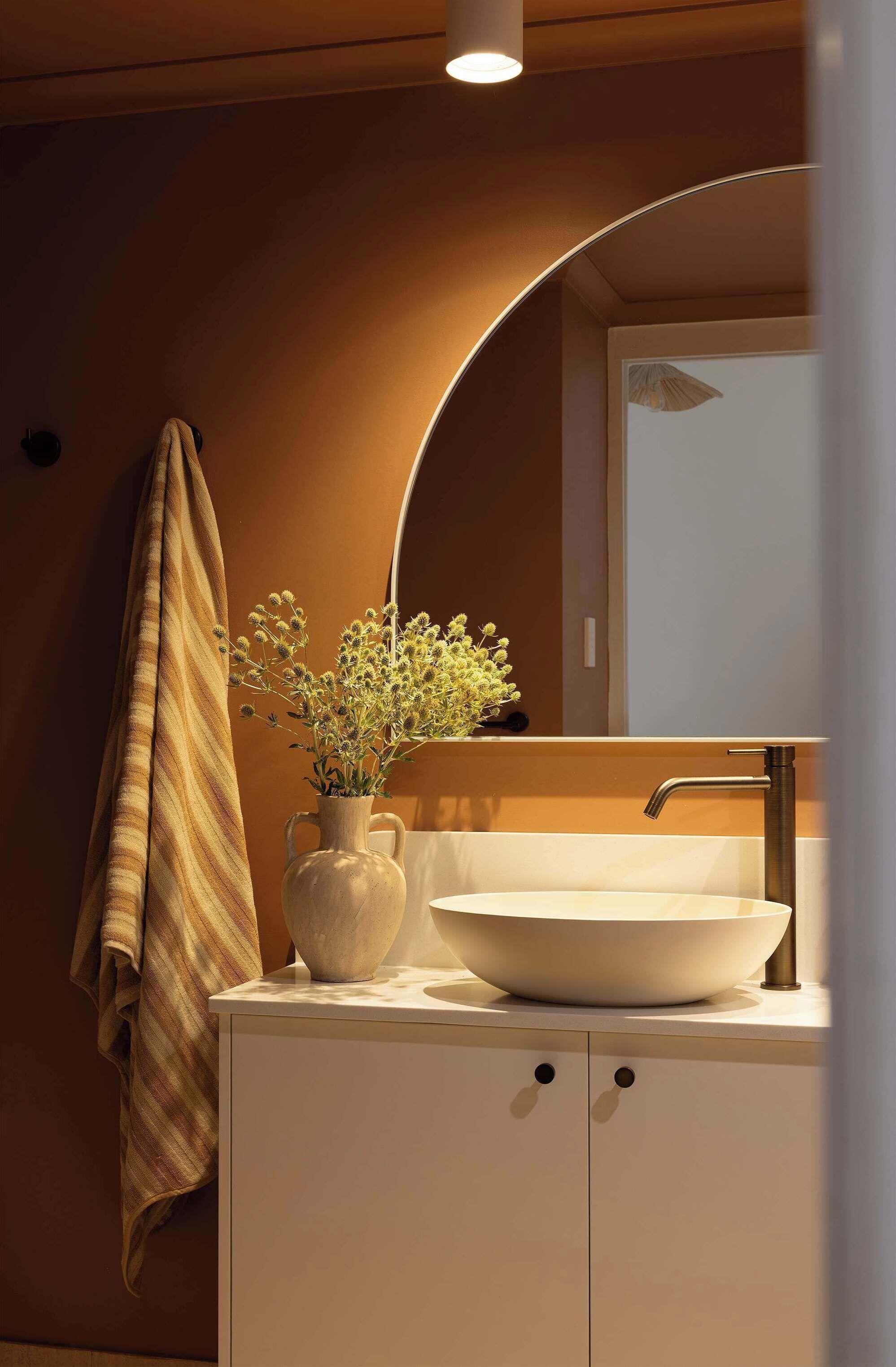 Un baño con un lavabo blanco, un espejo y un florero con flores.