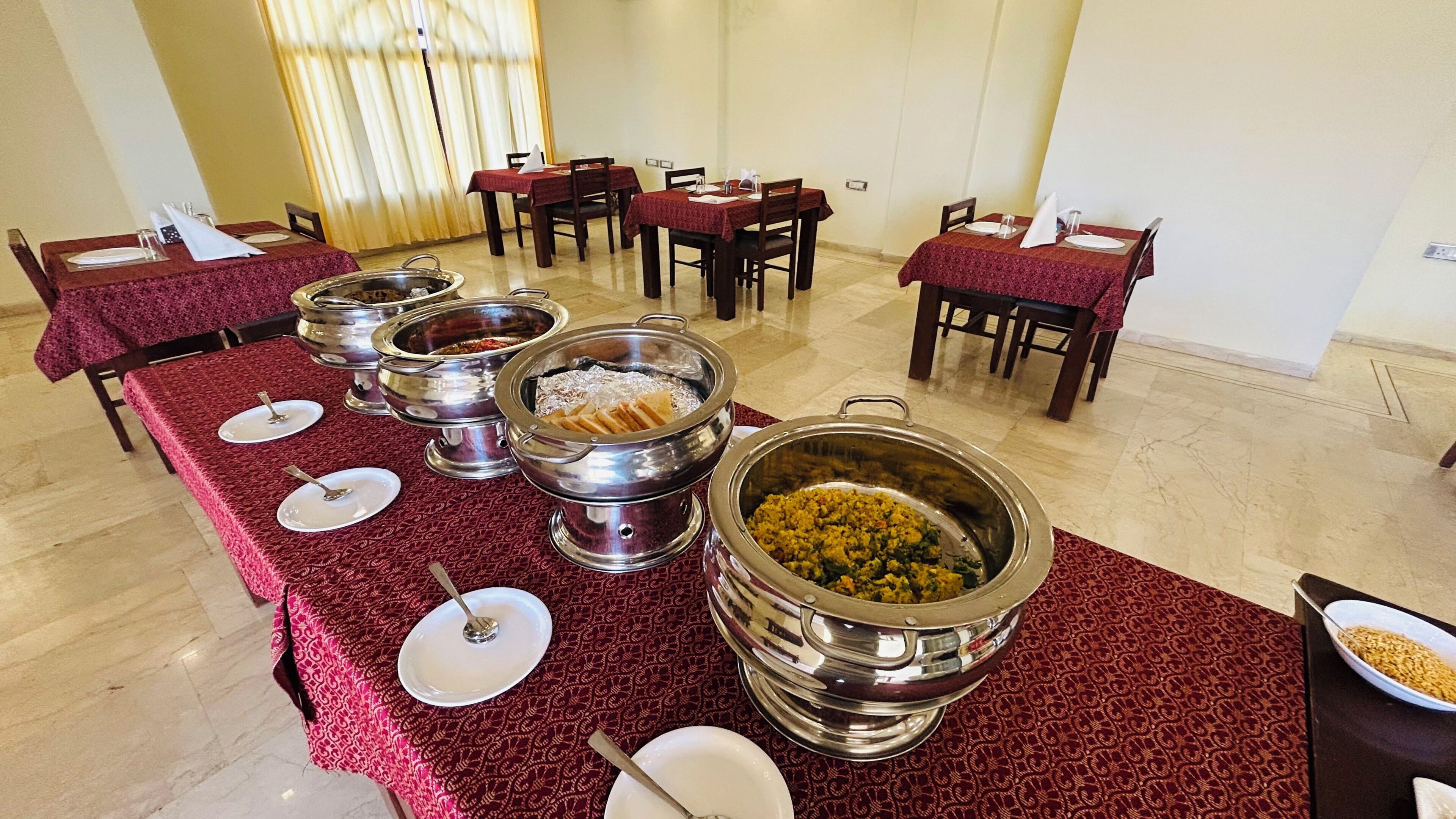 A buffet setup with multiple stainless steel serving dishes on a red tablecloth-covered table.