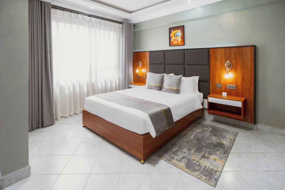 Een moderne hotelkamer met een groot bed, een nachtkastje, een wandlamp en een raam met gordijnen.