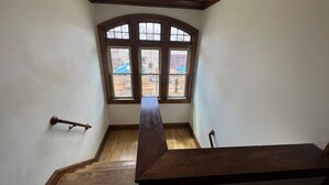 A room with a wooden staircase, a large arched window, and a view of an outdoor play area. - Babich Building - 3 Bedroom - Upper Apt #4 (West Allis)