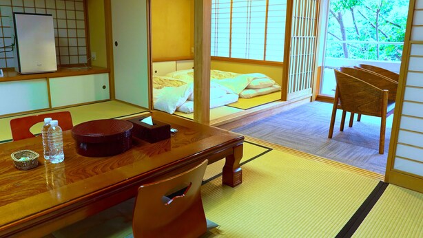 A traditional Japanese room with tatami flooring, a low wooden table, and a bed with futon mattresses. - ATAMI KAKUREZATO (Atami)