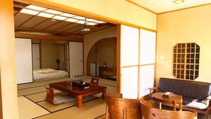 A traditional Japanese room with tatami flooring, a low wooden table, a sofa, and a sliding door leading to a bedroom. - ATAMI KAKUREZATO (Atami)
