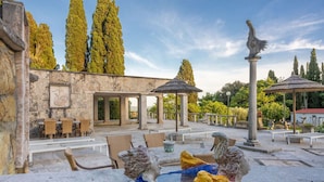 Un espace extérieur aménagé avec des tables et des chaises en pierre, une fontaine en pierre et une pergola.