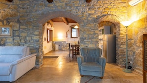 Un intérieur aux murs de pierre, avec un canapé, un fauteuil et un coin repas.