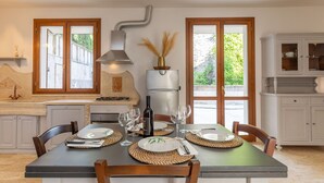A dining area with a table set for four, a gas stove, a range hood, and a view of greenery outside. - Dependance 2 - Holiday Rental with swimming pool on the Tuscan Coastline (Monteverdi Marittimo)