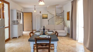 A dining area with a table set for four, a spiral staircase, and a kitchen with white cabinets. - Dependance 2 - Holiday Rental with swimming pool on the Tuscan Coastline (Monteverdi Marittimo)